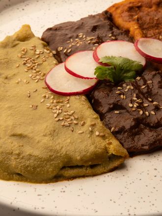 Enmoladas de pipián verde y mole en un plato blanco