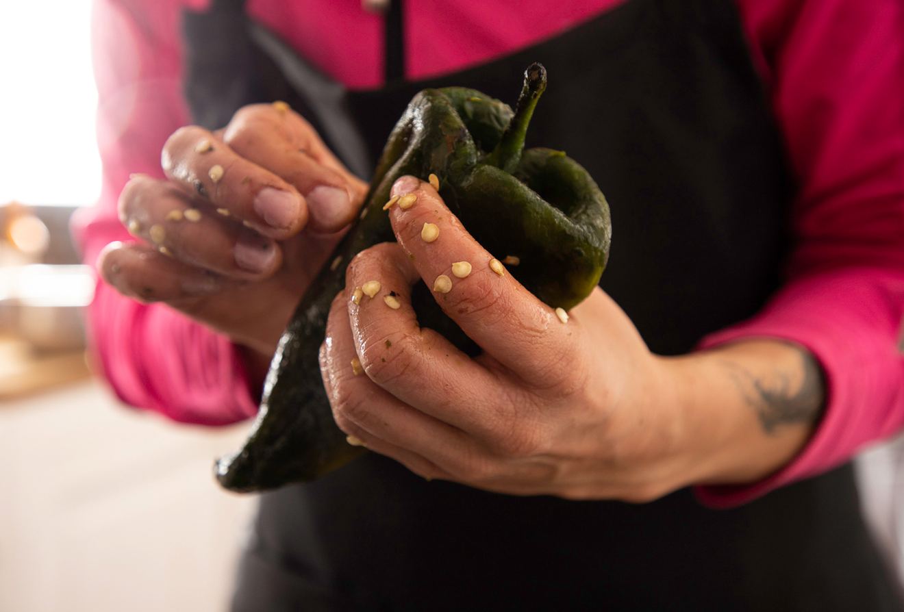 Unas manos sostienen dos chiles poblanos recién tatemados, con la piel todavía ampollada
